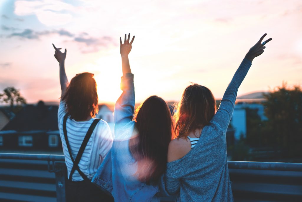 3 filles qui lèvent les bras avec vue sur une ville