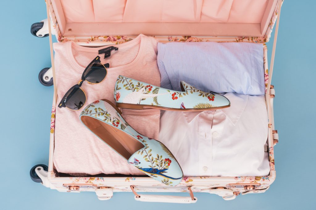 valise femme avec lunettes de soleil chaussures à fleurs et vêtements rose et bleu