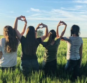 4 filles dans un champs qui forment des coeurs avec leurs mains