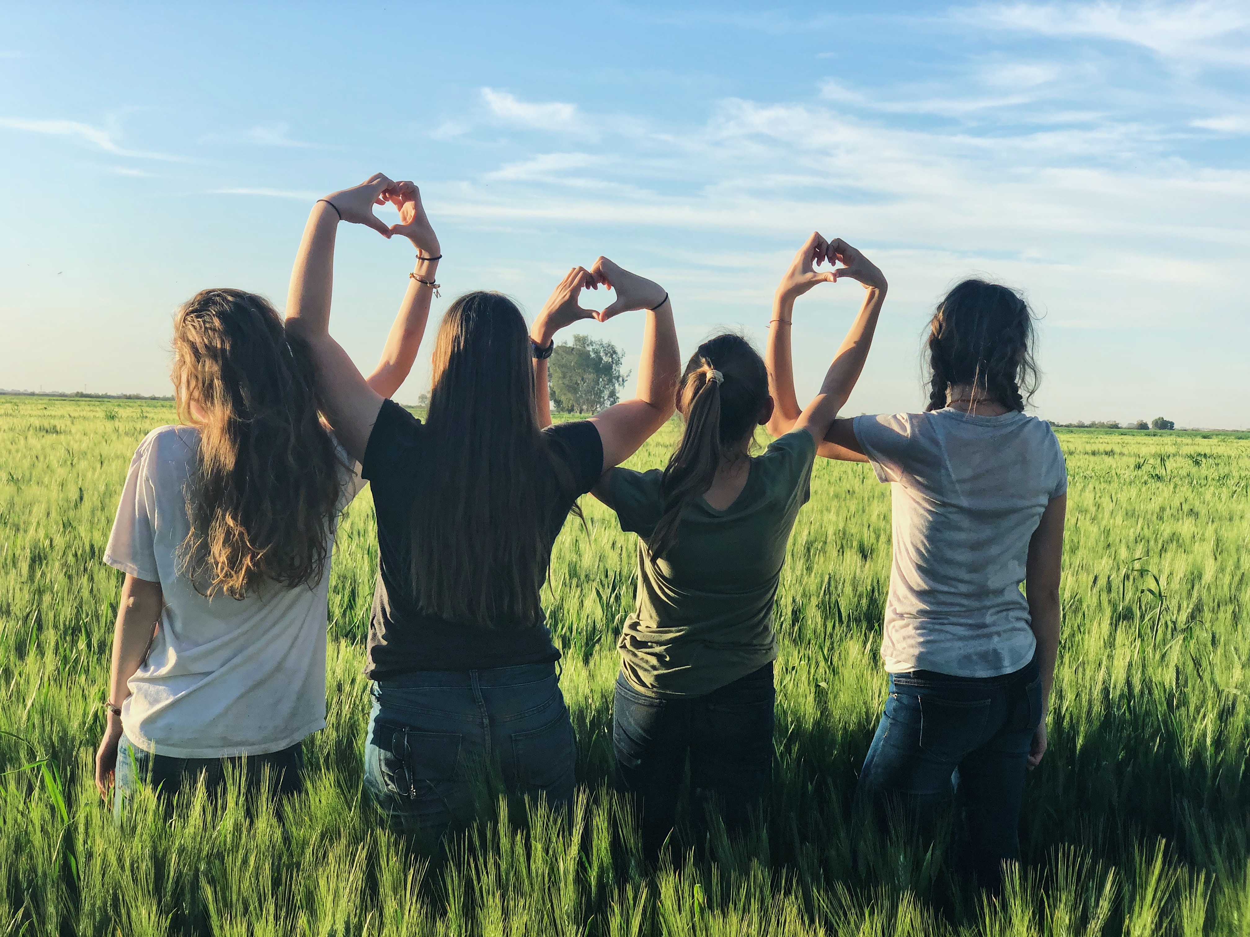 4 filles dans un champs qui forment des coeurs avec leurs mains