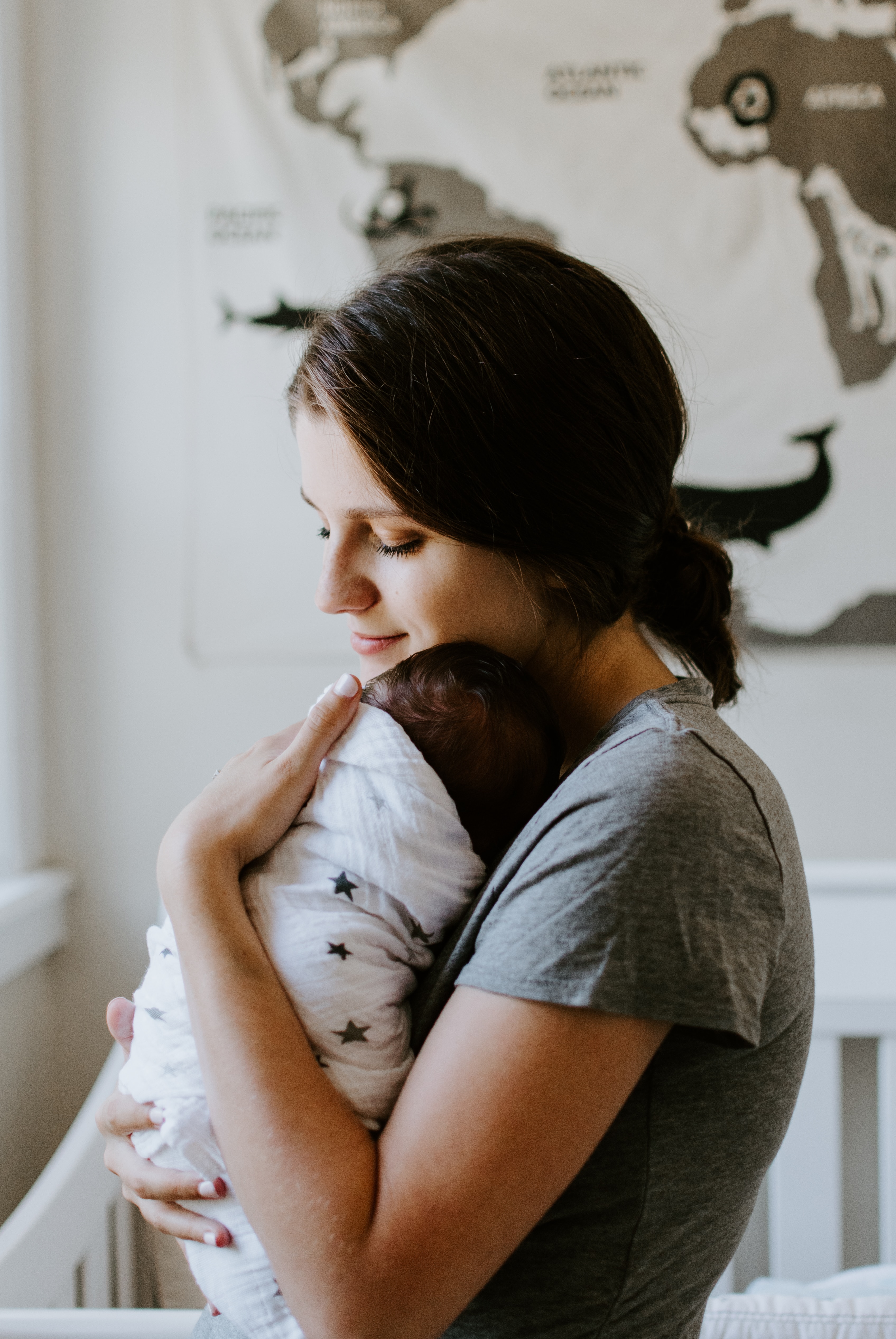 maman en t-shirt gris tenant son bébé recouvert d'une couverture dans ses bras