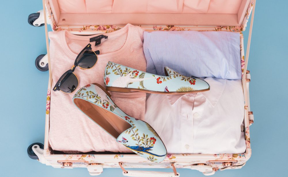 valise ouverte vue de dessus avec chaussures vêtements et lunettes de soleil