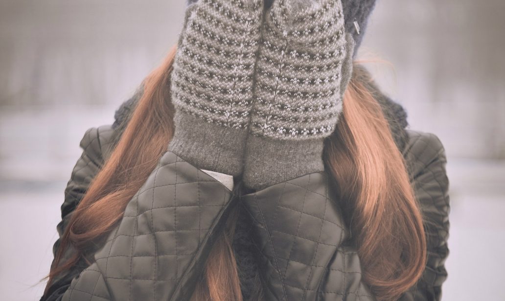 femme aux cheveux longs qui porte un bonnet et des moufles se cachant le visage