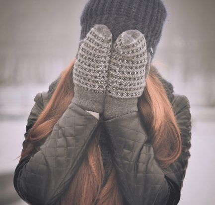 femme aux cheveux longs qui porte un bonnet et des moufles se cachant le visage